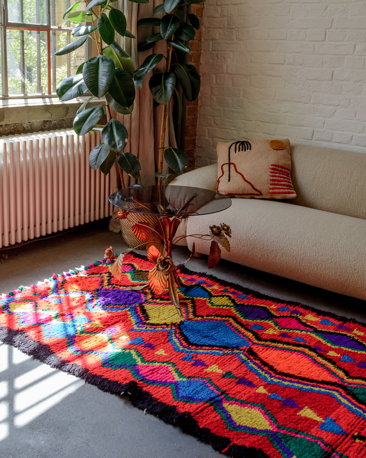 Colourful rug laying on the floor in front of a cream couch and sunny warehouse window.